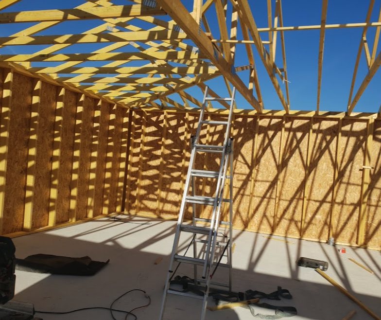 Charpente en fermettes bois posée sur une maison à ossature bois, vue de l’intérieur avec une échelle au centre