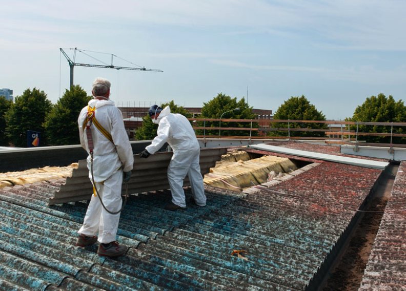 Deux intervenants en combinaison de protection retirant d’anciennes plaques ondulées sur une toiture
