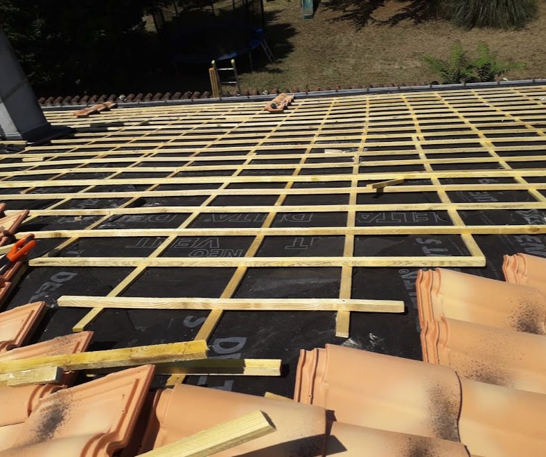 Pan de toiture recouvert d’un écran sous toiture noir et de liteaux bois, tuiles en attente au premier plan